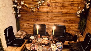 Ein gemütlicher Essbereich im Freien mit einem Holztisch, gedeckt für eine Mahlzeit, umgeben von Stühlen und Hockern.