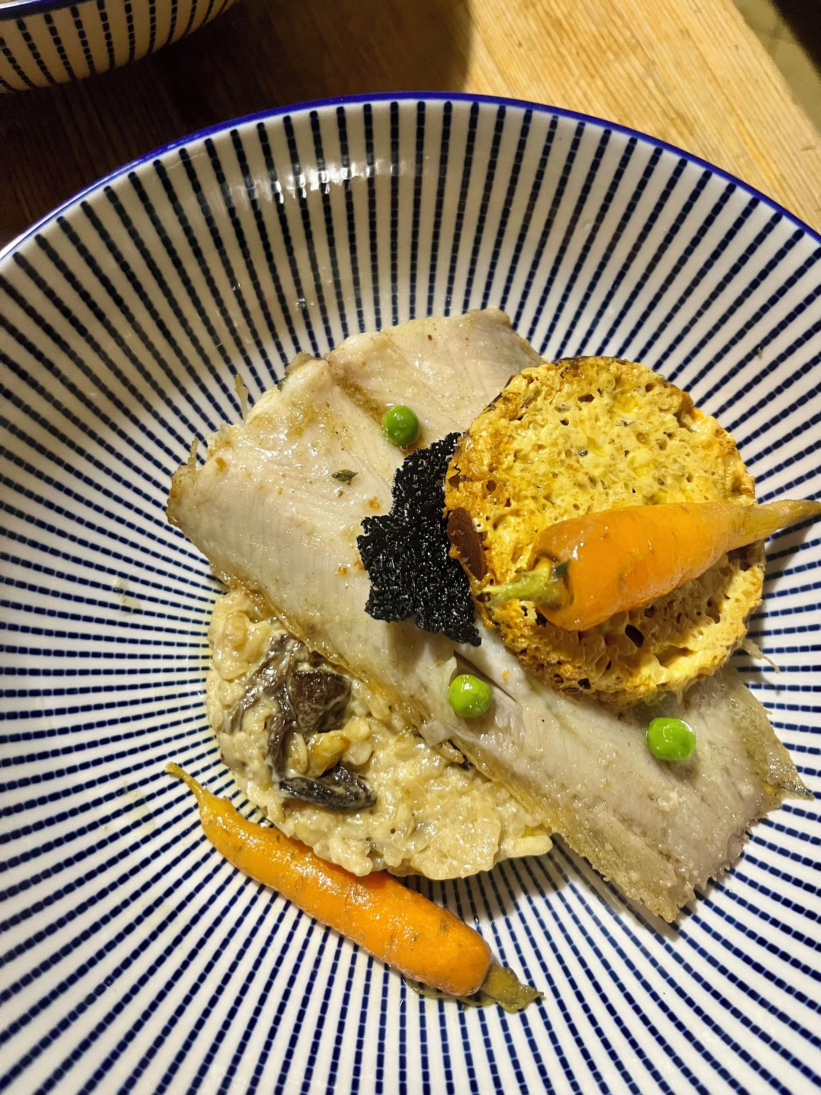 Une assiette contenant un morceau de viande, des petits pois, une carotte et une tranche de pain.