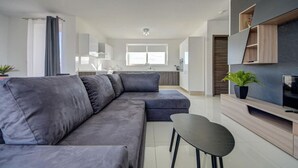Un soggiorno moderno con un divano angolare grigio, un tavolino nero e una TV su un mobile in legno.