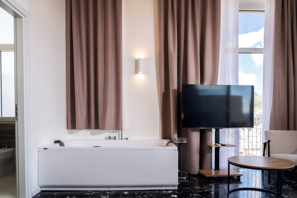A modern bathroom with a bathtub, a flat-screen TV, and a small round table. - Skyline Boutique Hotel (Palermo)