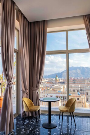 A room with two chairs and a table, large windows with curtains, a view of a cityscape and mountains. - Skyline Boutique Hotel (Palermo)