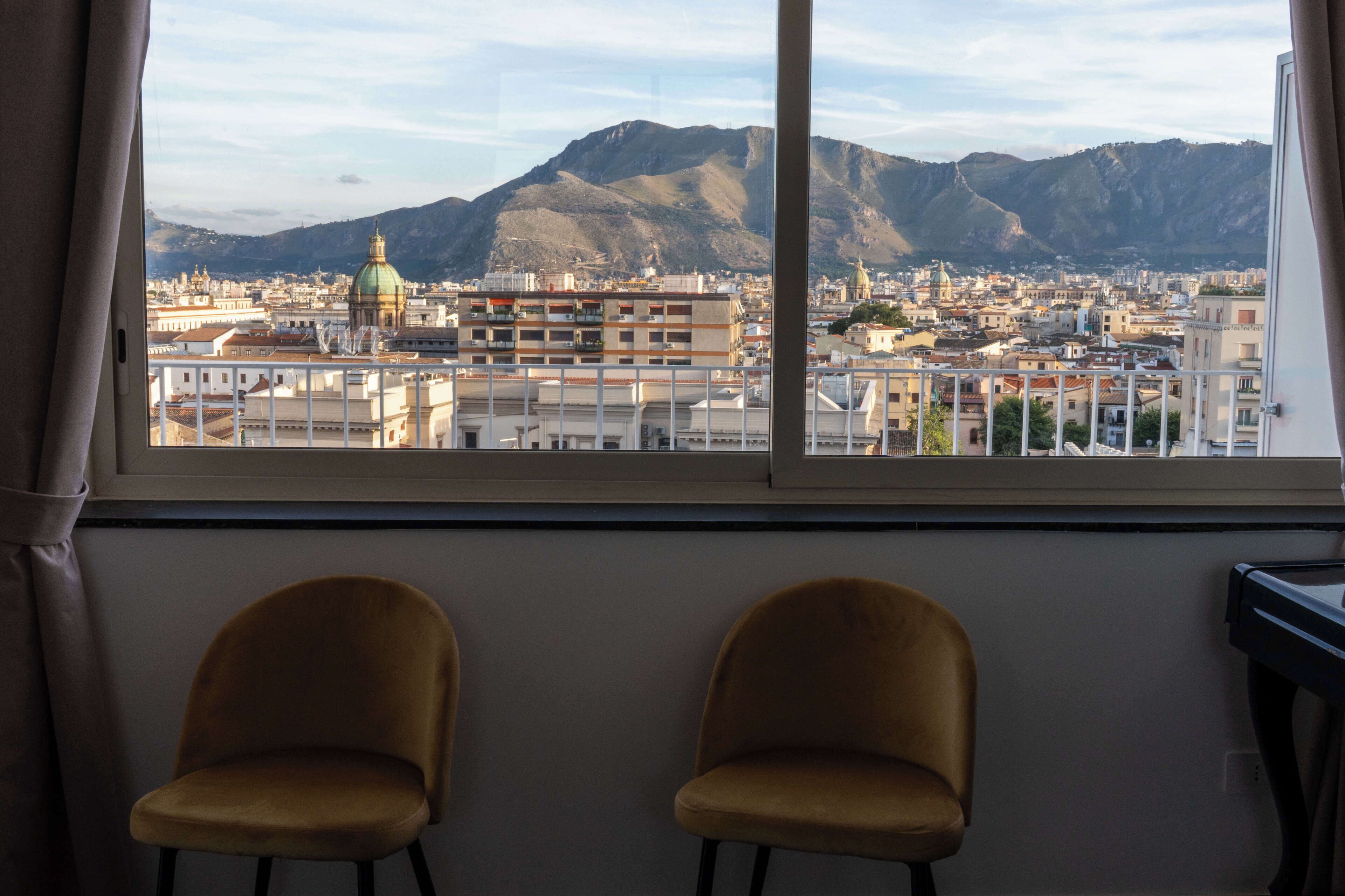 A room with two chairs facing a window overlooking a cityscape with mountains.