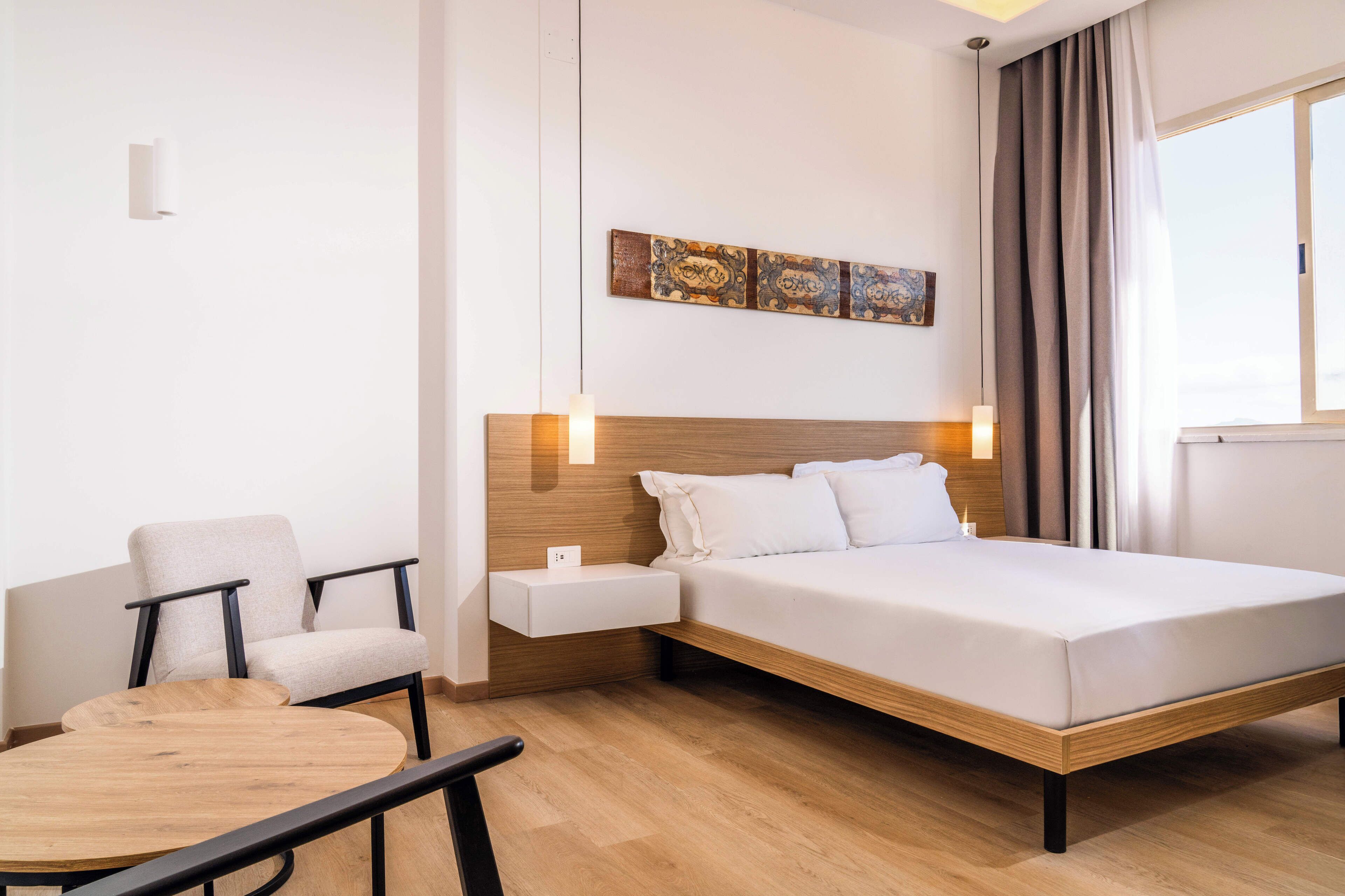 Una habitación de hotel moderna con una cama de madera, una mesa redonda, una silla y una mesita de noche.