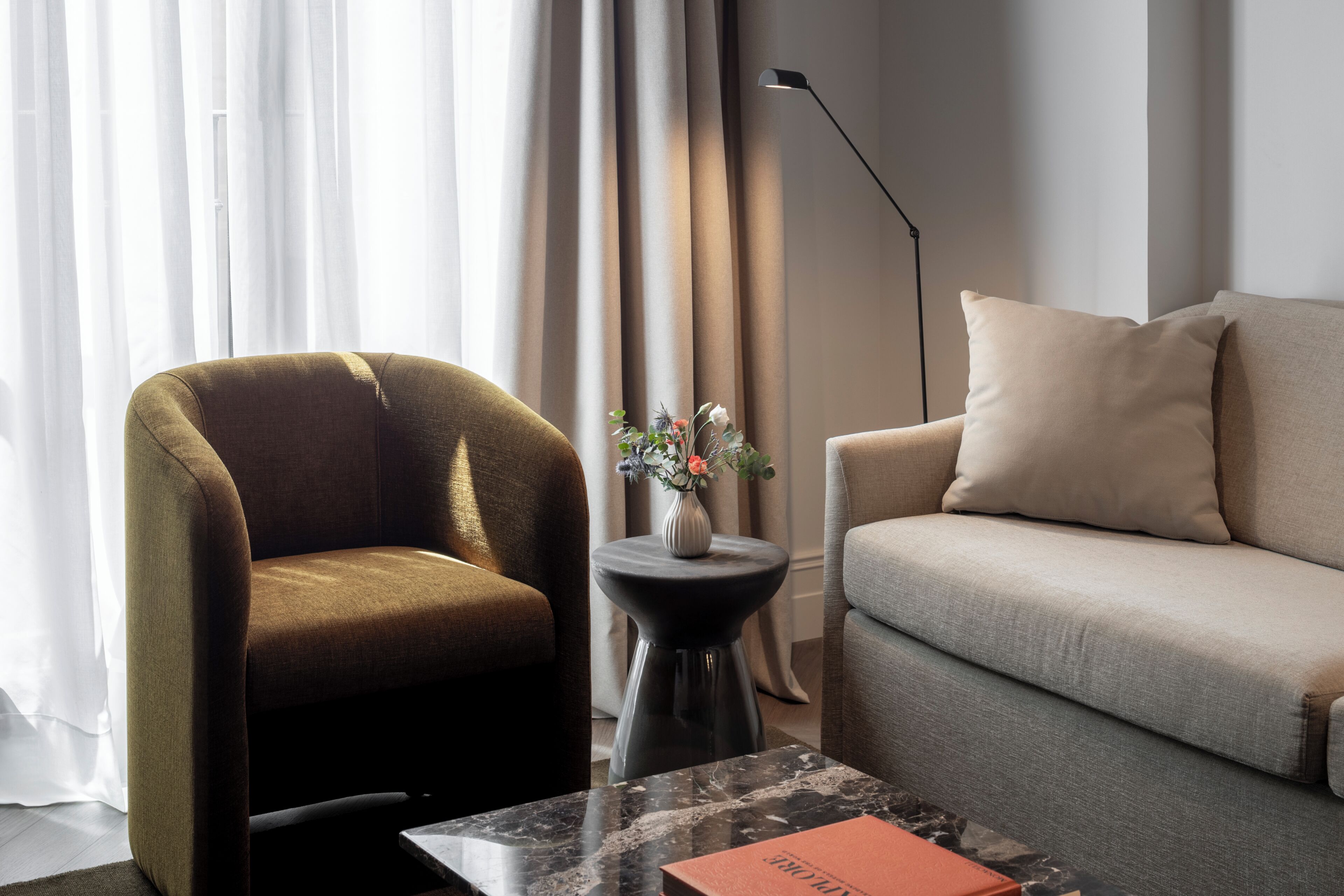 A modern living room with a sofa, armchair, and a small table with a vase.