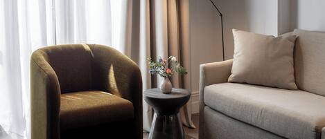 A modern living room with a sofa, armchair, and a small table with a vase.