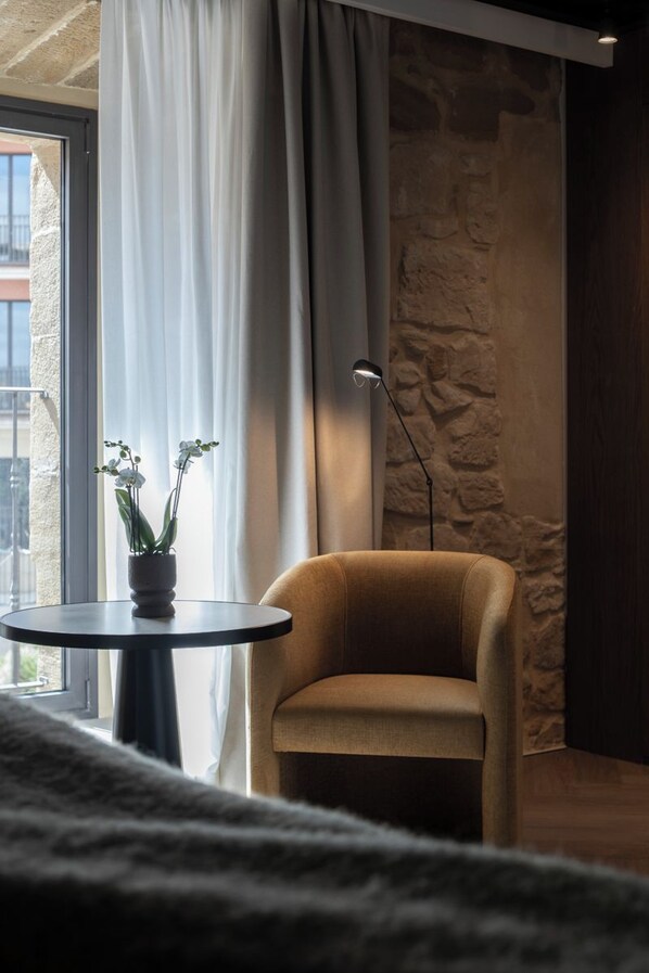 A room with a stone wall, a round table with a potted plant, a chair, and a floor lamp. - Hotel Palacio de los Angeles (Haro)