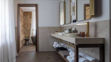 Un baño moderno con pared de piedra, una bañera, un tocador con grifo dorado y un espejo.