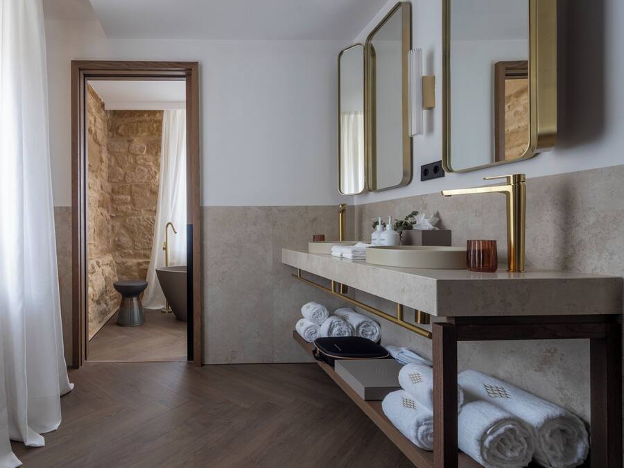 Un baño moderno con pared de piedra, una bañera, un tocador con grifo dorado y un espejo.