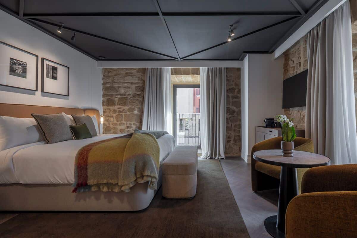 Una habitación de hotel moderna con una cama, una mesita, una silla, un sofá y una pared de piedra.
