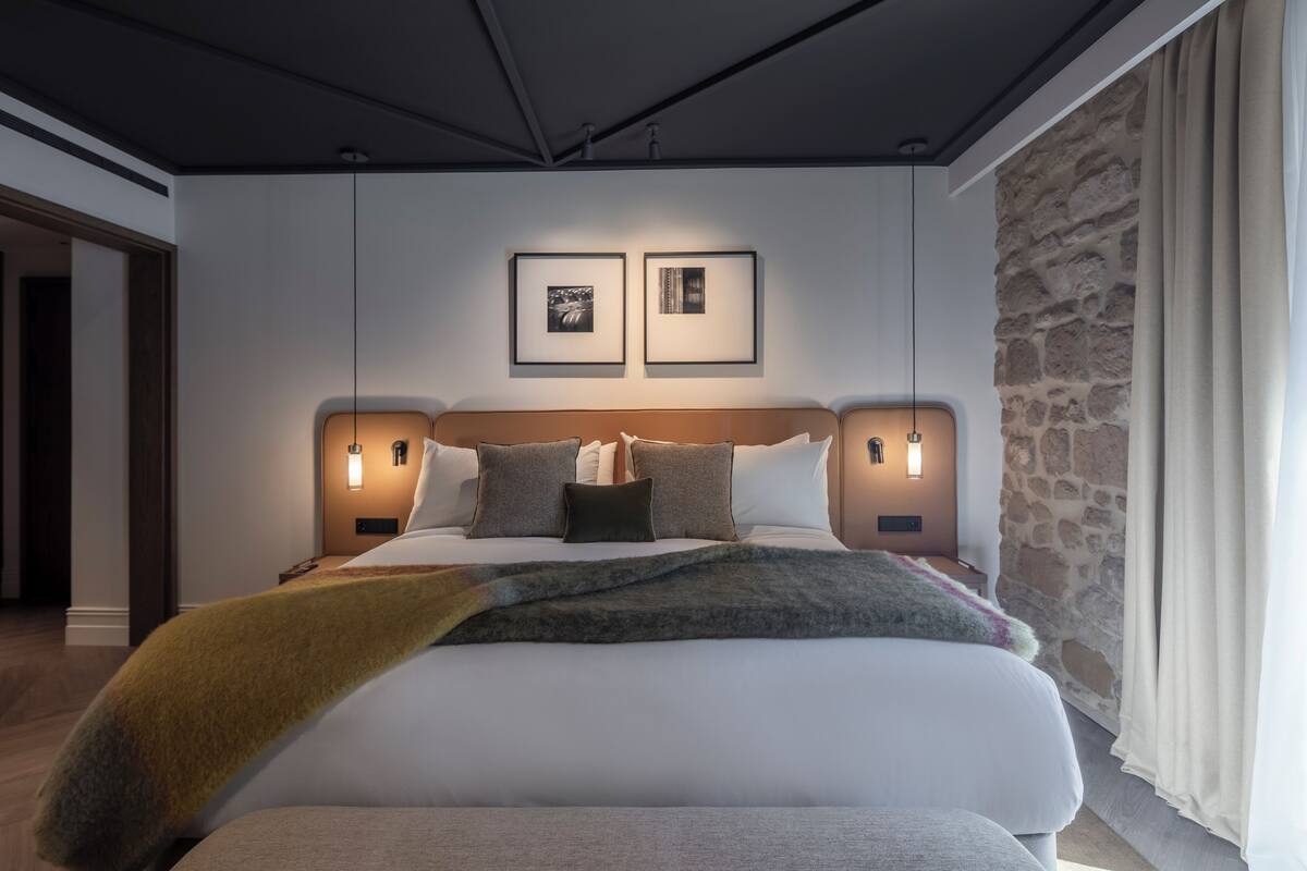 Un dormitorio moderno con una cama grande, dos luces fijadas a la pared y una pared decorativa de piedra.