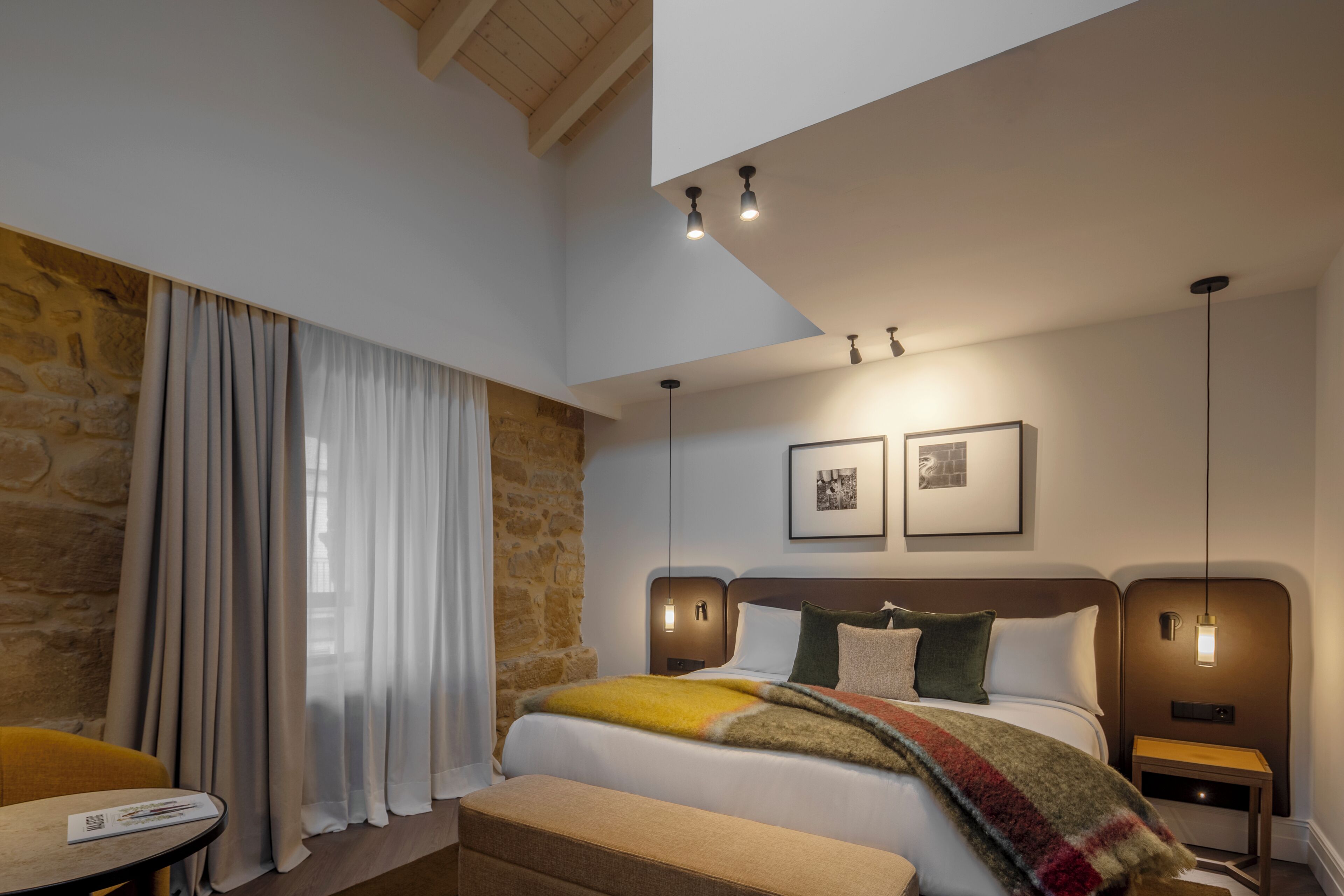 A hotel room with a bed, a small table, a chair, a nightstand, and a wall-mounted picture.