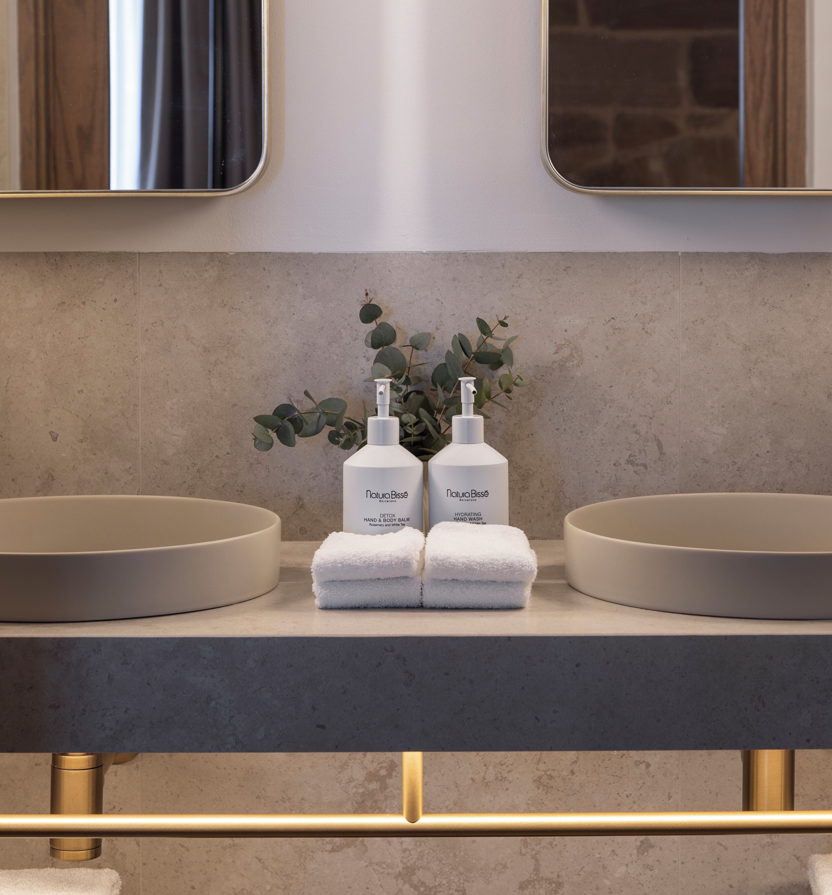 Un tocador de baño con dos lavamanos, un espejo y dos botellas de productos para el cuidado de manos Natura Bisse.