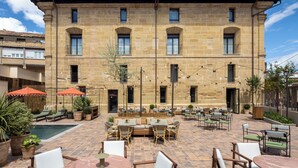 A courtyard with outdoor seating, a pool, and a stone building with multiple windows.