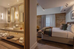 Ett modernt hotellrum med en stor säng, ett badrum med handfat och speglar samt en accentvägg klädd i sten.