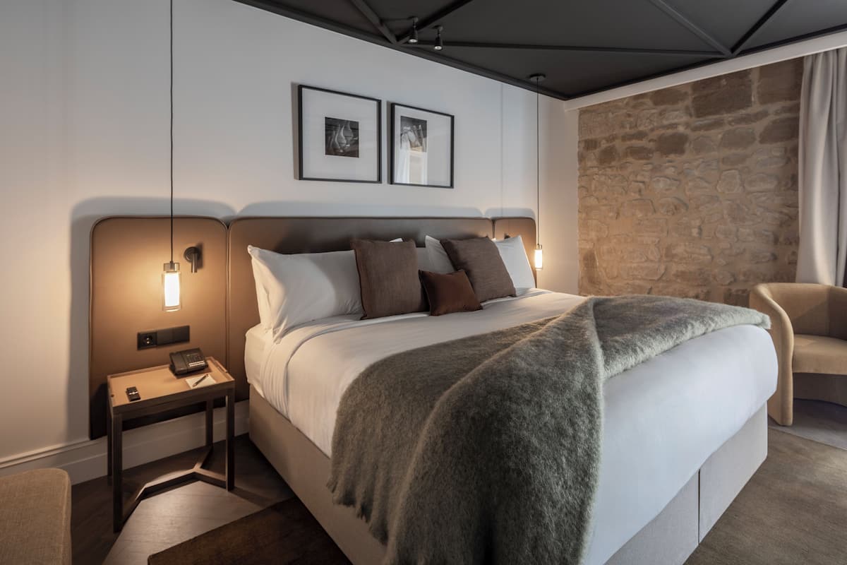 Una habitación de hotel moderna con una cama grande, dos mesitas de noche, una pared de acento de piedra y una silla.
