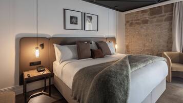 Camera d'albergo moderna con un letto grande, due comodini, una parete decorata in pietra e una sedia.