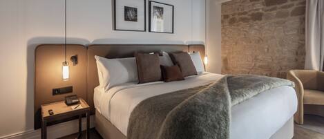 Una habitación de hotel moderna con una cama grande, dos mesitas de noche, una pared de acento de piedra y una silla.