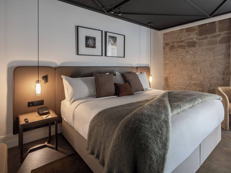 Camera d'albergo moderna con un letto grande, due comodini, una parete decorata in pietra e una sedia.