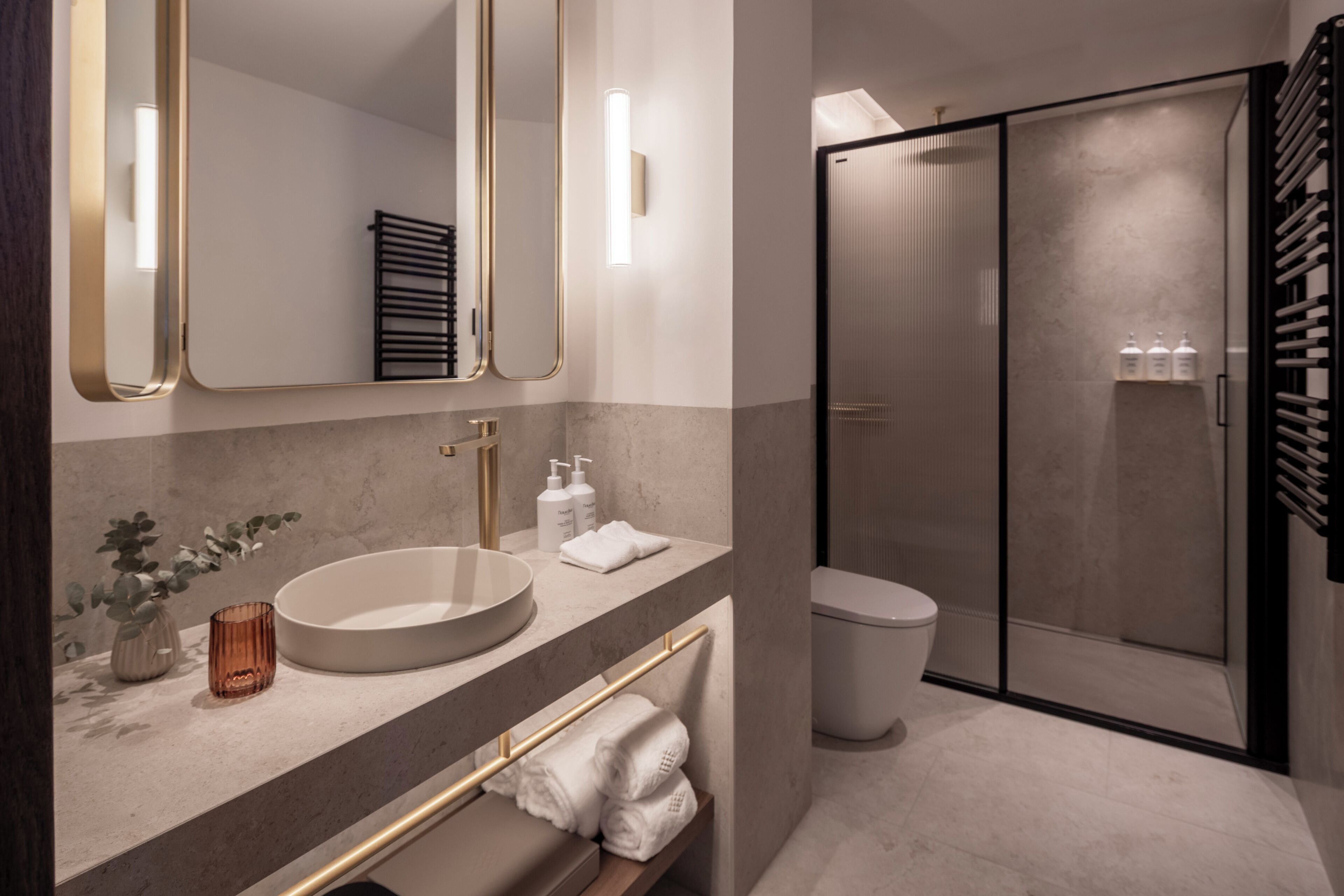 A modern bathroom with a round sink, a towel rack, a toilet, and a glass shower enclosure.