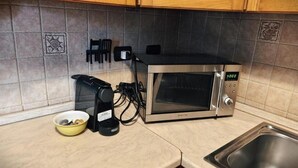 Una cocina con microondas, cafetera y un tazón sobre la encimera.