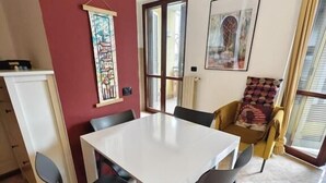 Un comedor con una mesa blanca y cuatro sillas, una pared de acento roja y dos ventanas con persianas.