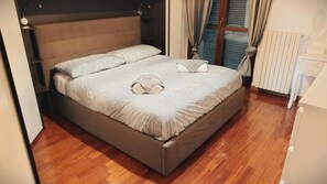 Una cama bien hecha con cabecera, mesita de noche y radiador.