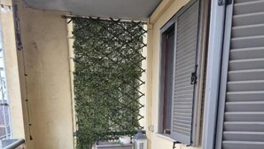 Un pequeño espacio al aire libre con una mesa y sillas de madera, una planta en maceta y un cojín azul en el suelo.