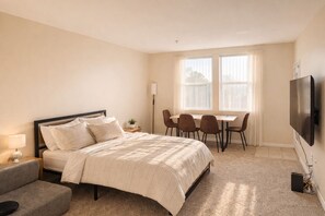 Ein Schlafzimmer mit Bett, Nachttisch, Lampe, Stuhl, Schreibtisch und Fernseher.