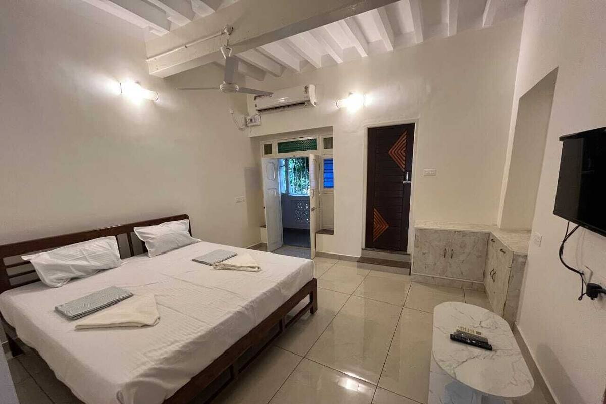Habitación de hotel con una cama grande, una mesita de noche pequeña, un televisor montado en la pared y una puerta que da al baño.