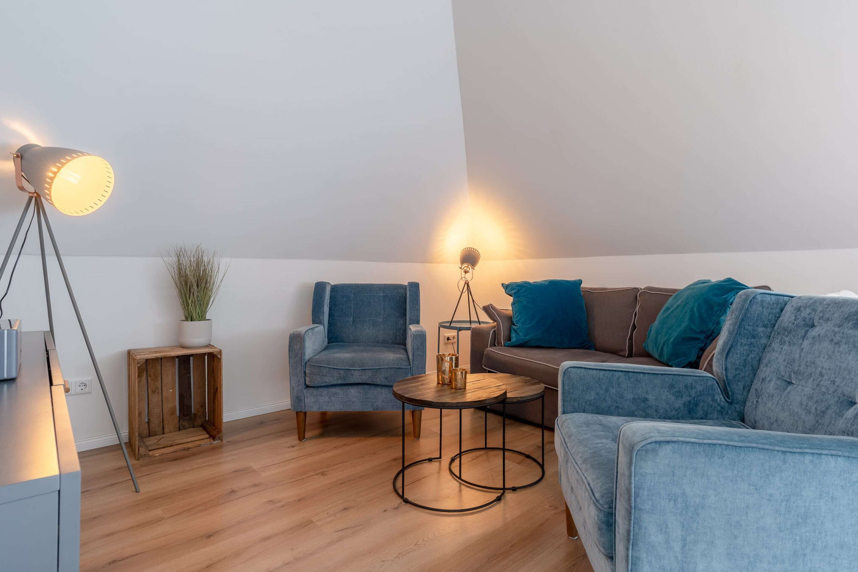 A modern living room with a blue sofa, a blue armchair, a small wooden side table, and a floor lamp.
