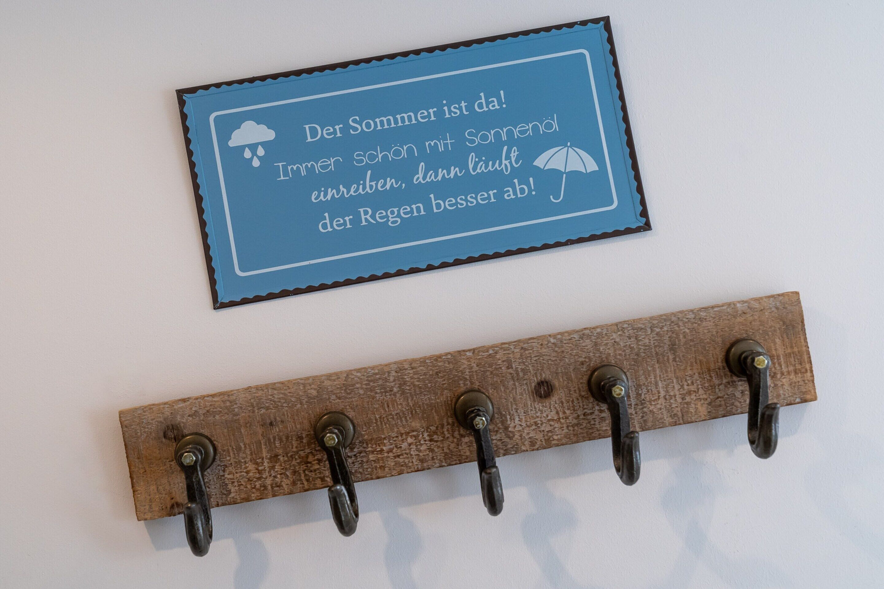 A wall-mounted sign with a message in German, and a wooden coat rack with hooks.