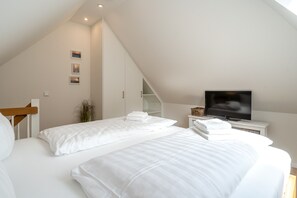 A bedroom with two beds, a TV, and a staircase leading to an upper level. - Ferienwohnung in St.peter Ording (St. Peter-Ording)