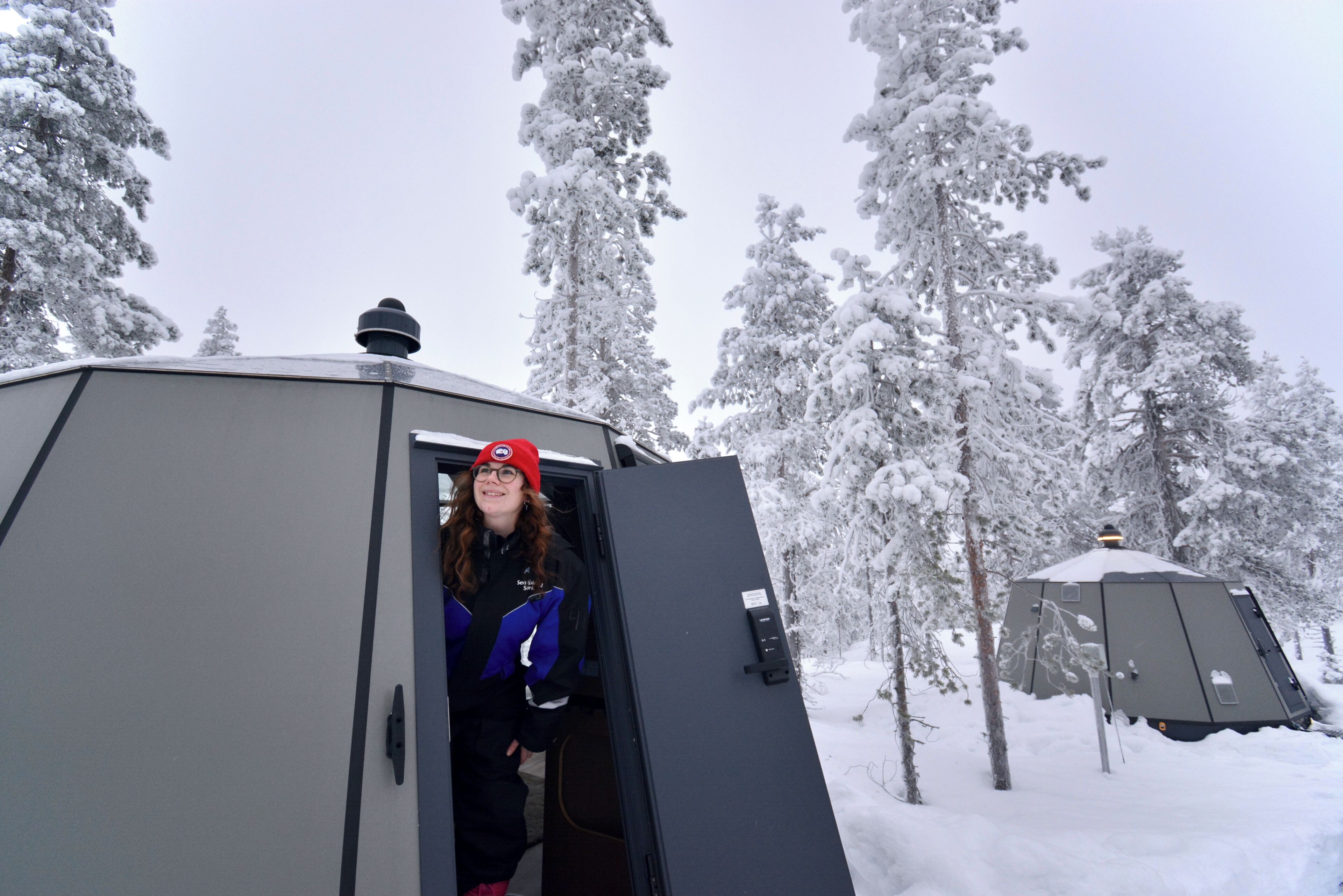 A large, metallic, snow-covered structure with a door open, surrounded by snow-laden trees.