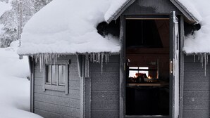 Ein mit Schnee bedecktes Blockhaus mit Schornstein, einer einladenden Tür und Eiszapfen am Dach.