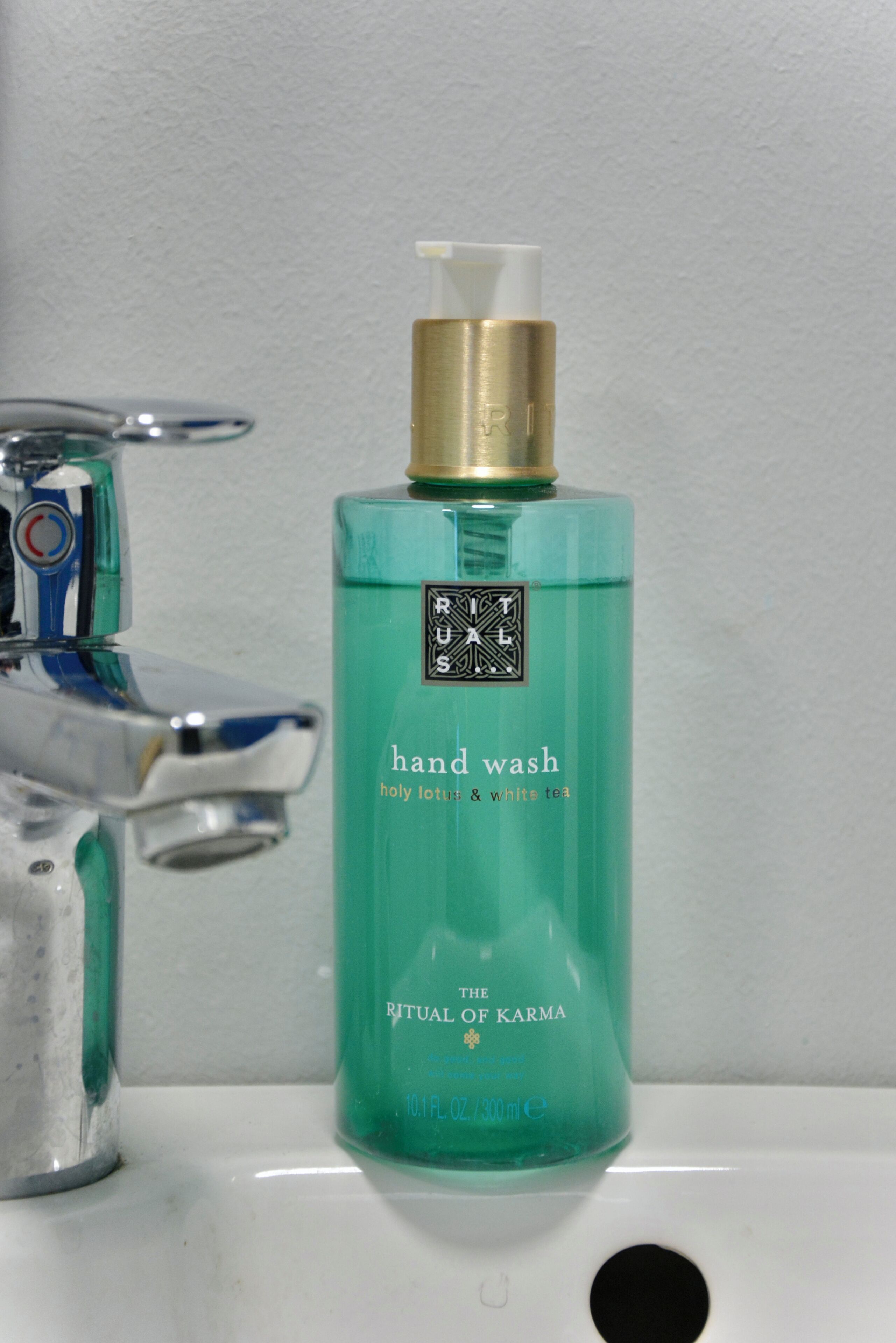 A bathroom sink with a hand wash bottle labeled "The Ritual of Karma" next to a faucet.