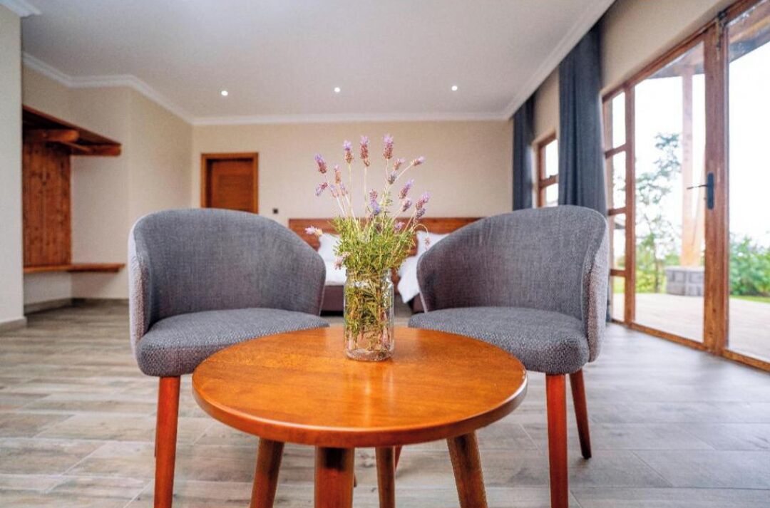 A room with two grey upholstered chairs facing a round wooden table with a vase of flowers.