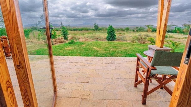 Une terrasse ouverte donnant sur un champ verdoyant et des montagnes lointaines, sous un ciel nuageux.
