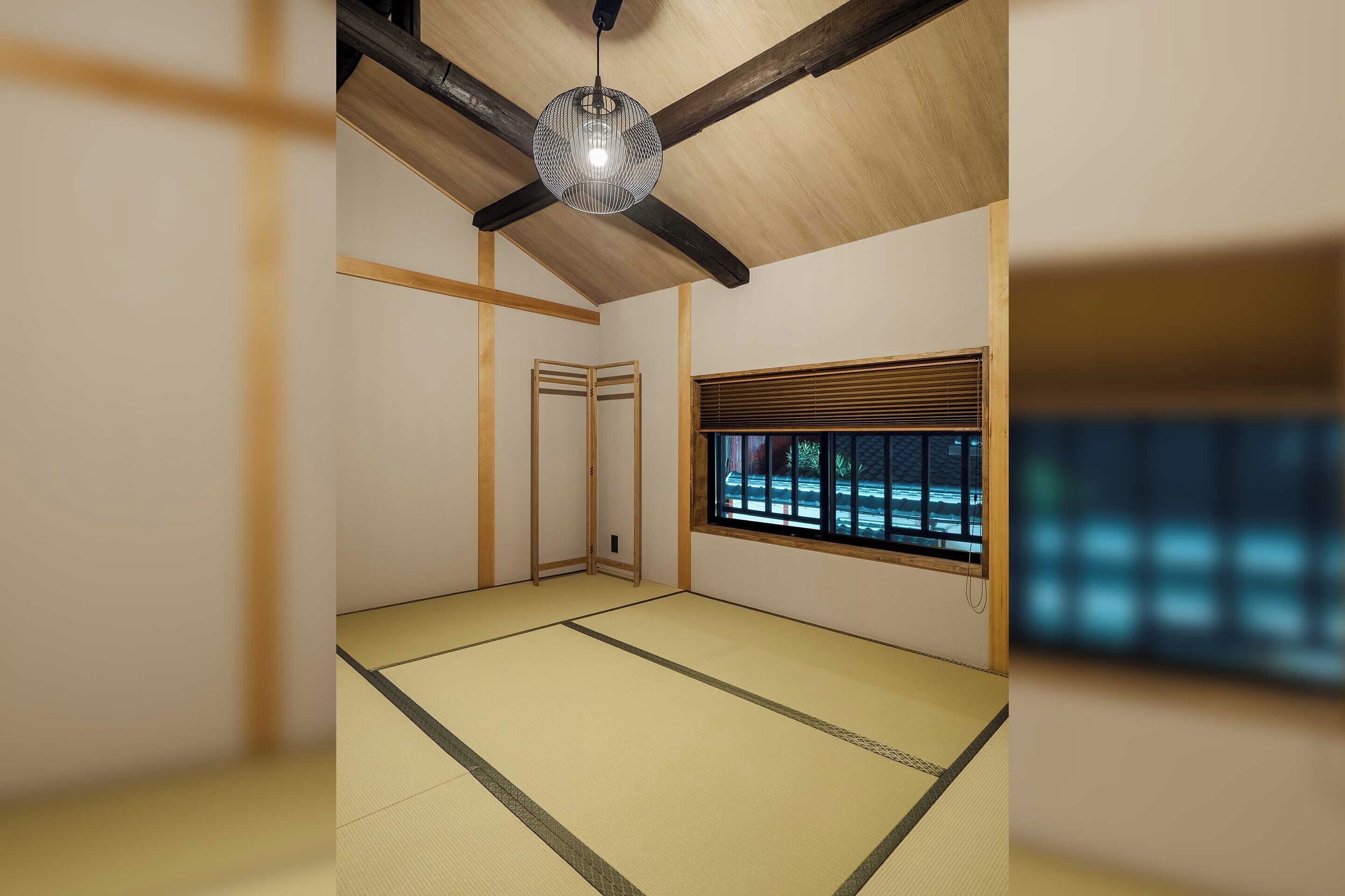 A traditional Japanese room with tatami flooring, a ceiling fan, a window with blinds, and a hanging light fixture.