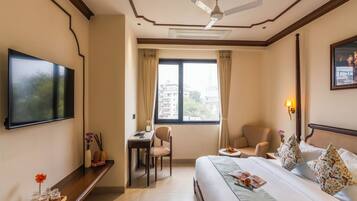 A hotel room with a bed, a desk, a chair, a TV, and a window with curtains.