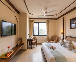 A hotel room with a bed, a desk, a chair, a TV, and a window with curtains.
