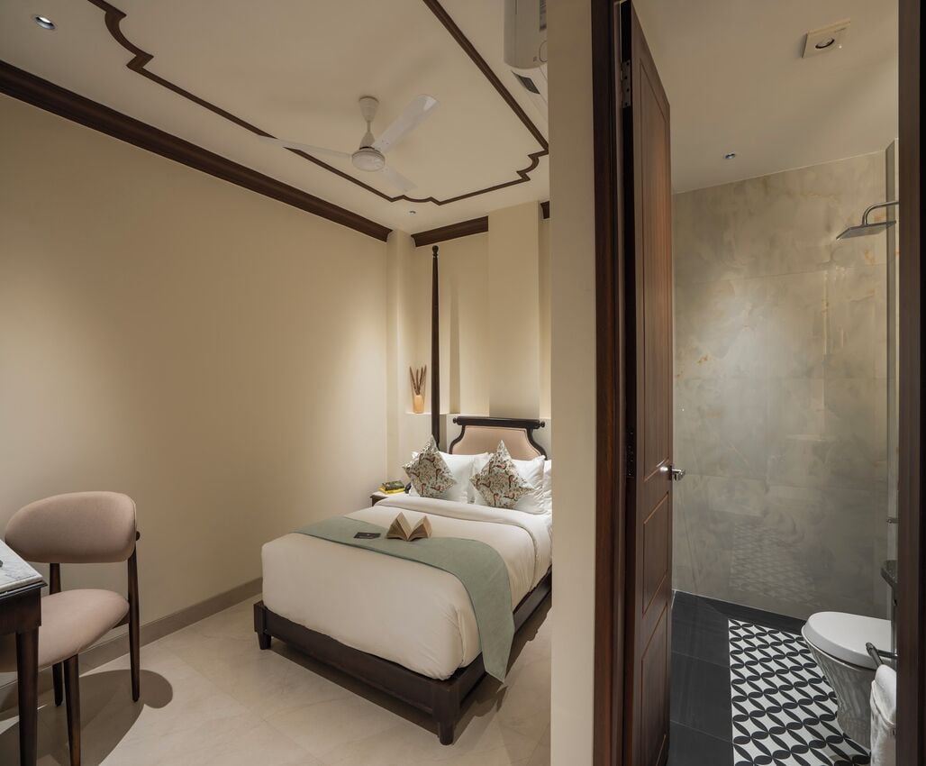 A hotel room with a bed, a desk, a chair, a bathroom with a shower, and a toilet.