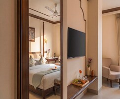 Une chambre d’hôtel avec un lit, un téléviseur fixé au mur, un coin salon avec un fauteuil et une petite table sur laquelle se trouve un plateau de fruits.
