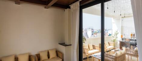 A spacious balcony with wicker furniture, a dining area, and a view of the cityscape.