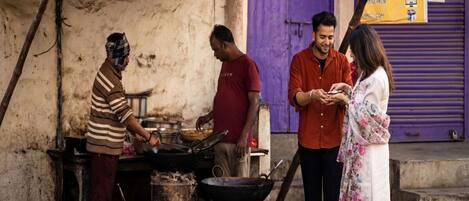 A street food vendor cooking at a makeshift stall with a purple building in the background.