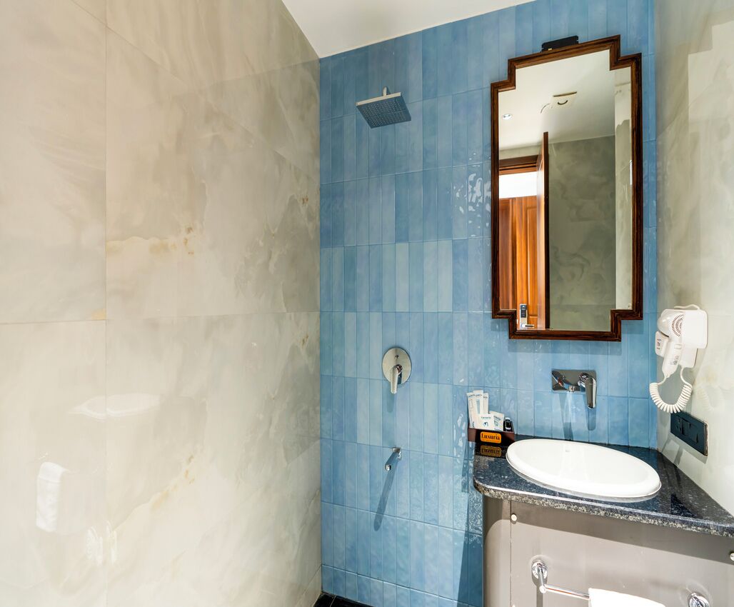 A bathroom with a blue tiled wall, a white sink, a mirror, and a towel rack.
