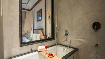 Un baño con un espejo grande, una bañera, una ducha y una bandeja de madera con una copa de vino tinto y fresas.