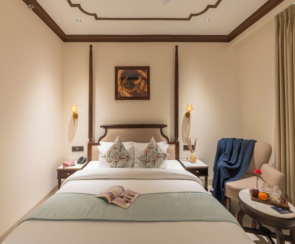 A hotel room with a large bed, two bedside tables, a chair, a small table with a tray of fruit, and a painting on the wall.
