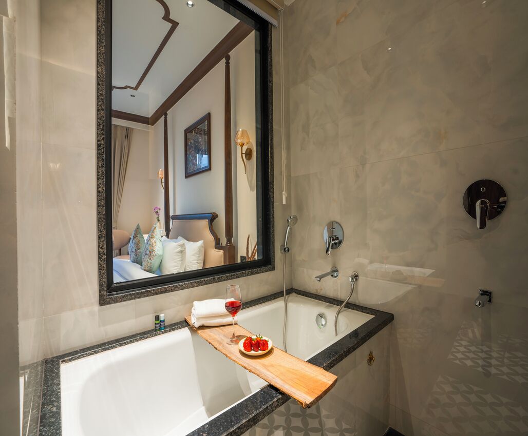 Un bagno moderno con uno specchio grande, una vasca da bagno, una doccia e un vassoio di legno con un bicchiere di vino e fragole.