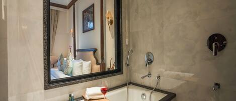Un bagno moderno con uno specchio grande, una vasca da bagno, una doccia e un vassoio di legno con un bicchiere di vino e fragole.