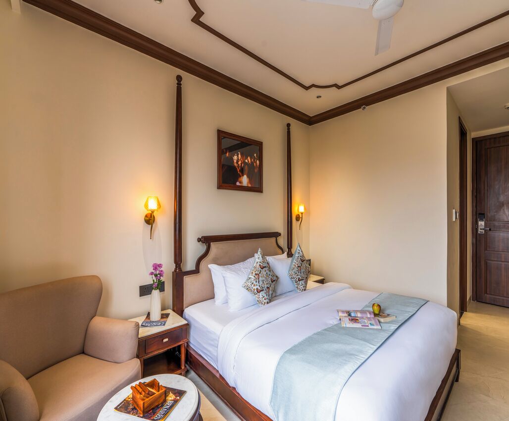 A hotel room with a bed, bedside table, lamp, and a chair.